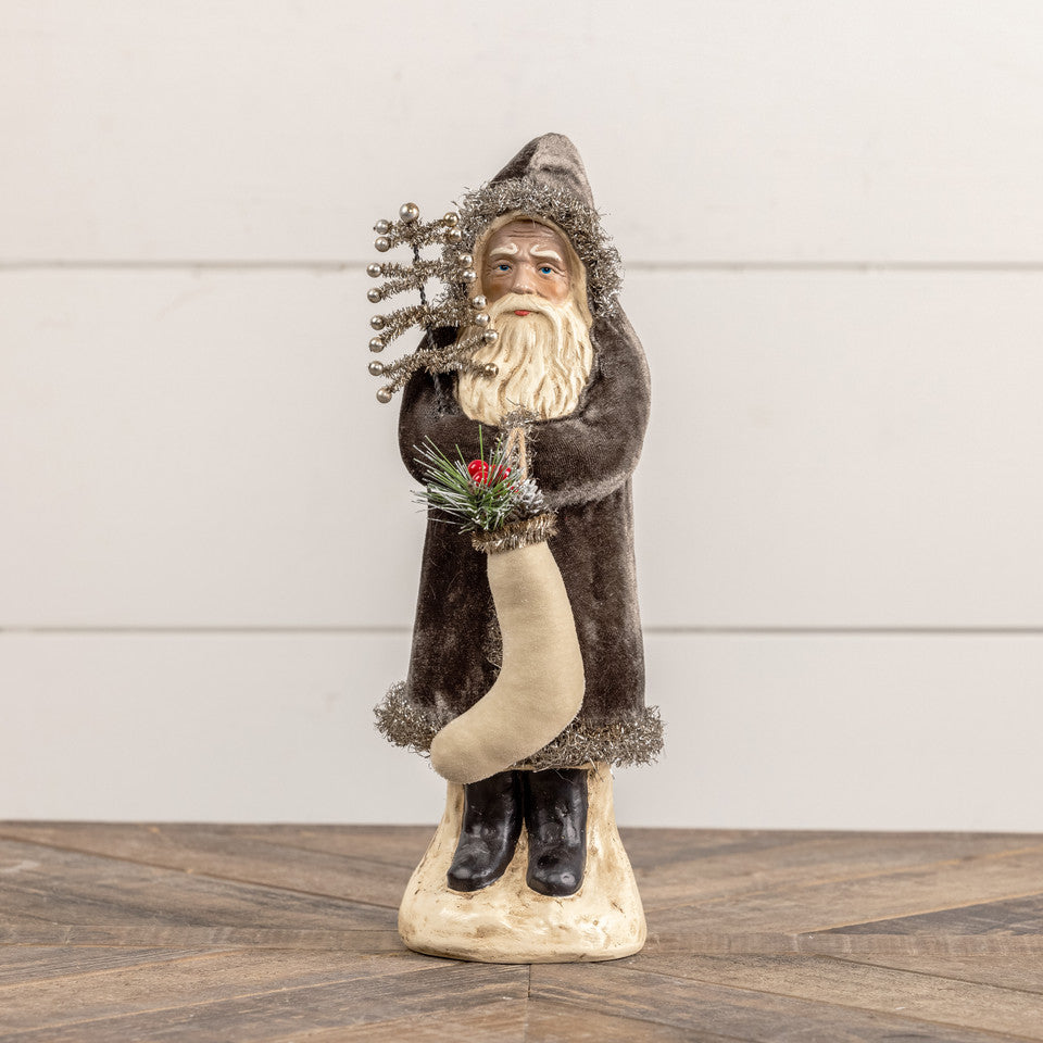 Decorative figure of a bearded man in a brown coat with a white beard, holding a red flower, on a wooden floor.