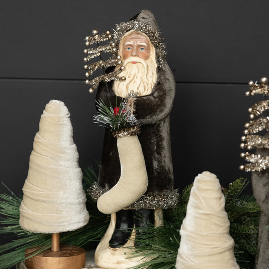 Decorative figure of a bearded man with a long white beard, wearing a fur coat, standing between two small trees against a dark background.