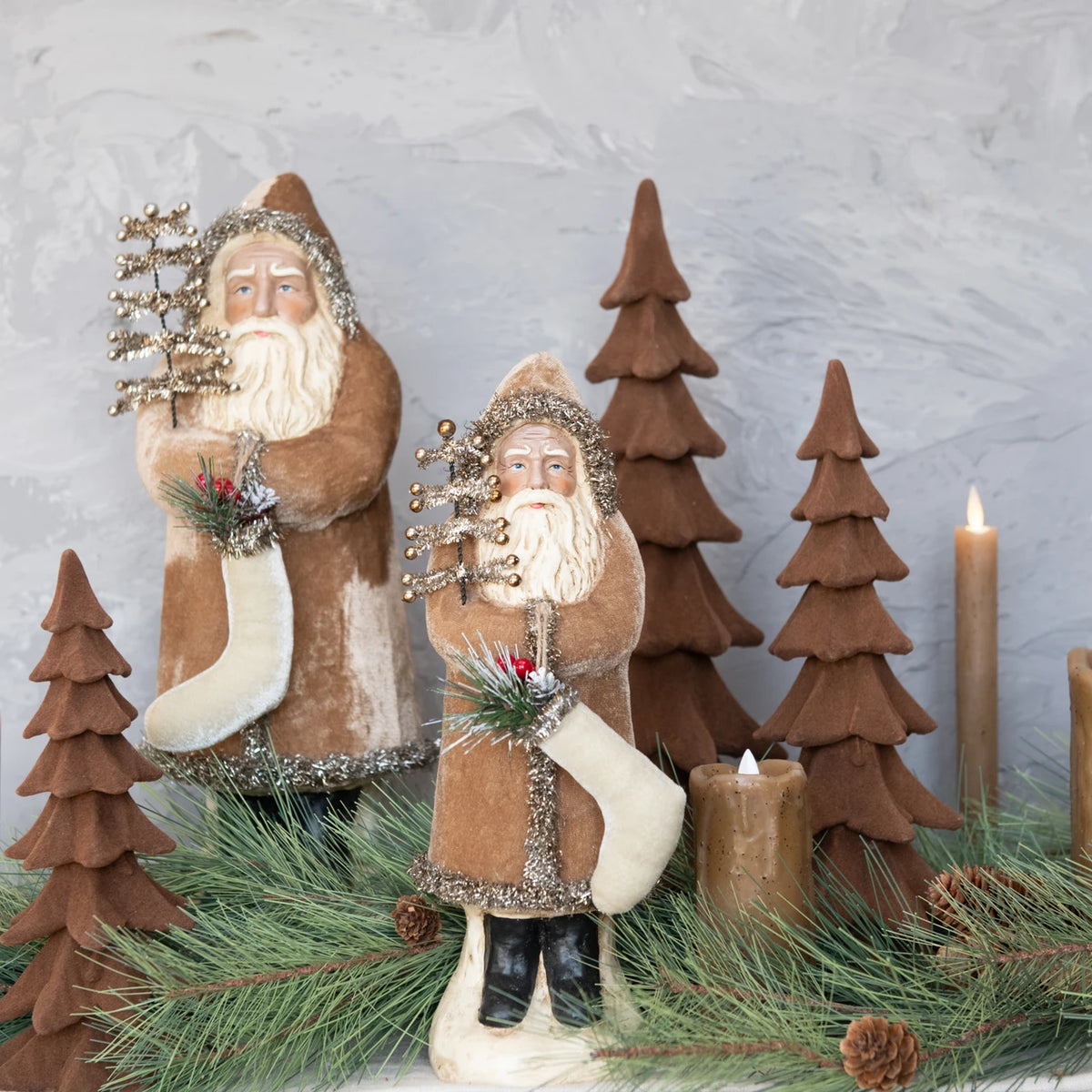 Two decorative Santa figures with trees and candles on a textured surface