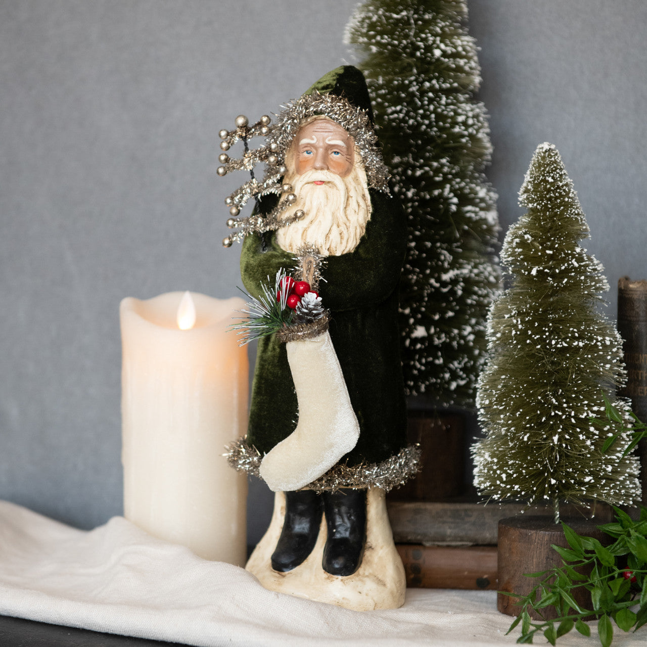 Decorative figure of a bearded man in a green coat with a candle and small trees in the background.