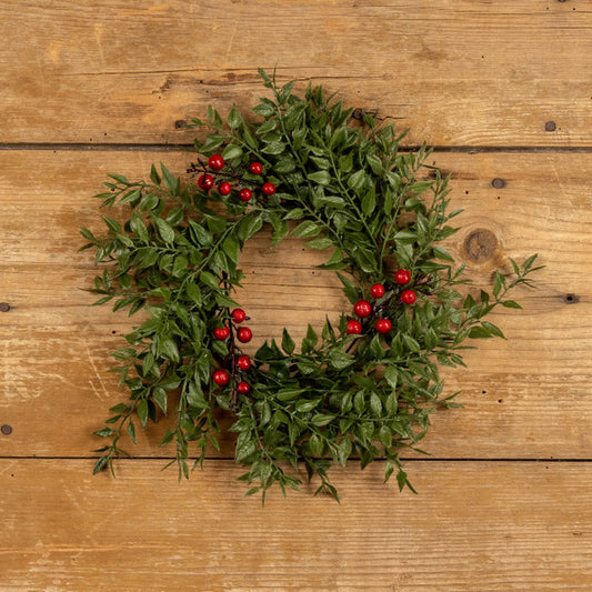 A round wreath made of green ferns with red berries, placed on a wooden surface.