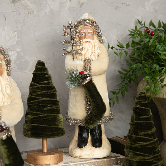 A decorative 12-inch oatmeal velvet belsnnickle figure wearing a Santa hat and a black coat, holding a miniature Christmas tree, standing next to another belsnnickle with a green coat and a Christmas tree.