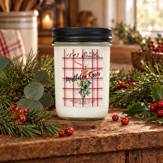 A white candle in a clear glass jar with a black lid sits on a rustic wooden table surrounded by green pine branches, eucalyptus leaves, and red berries. The front label has a red plaid pattern with the text '1609 Earth' and 'Middler Kross' plus a holly illustration.