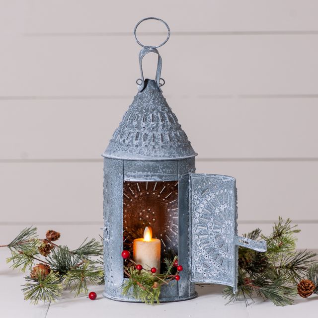 Decorative metal lantern with a lit candle, surrounded by greenery on a light background