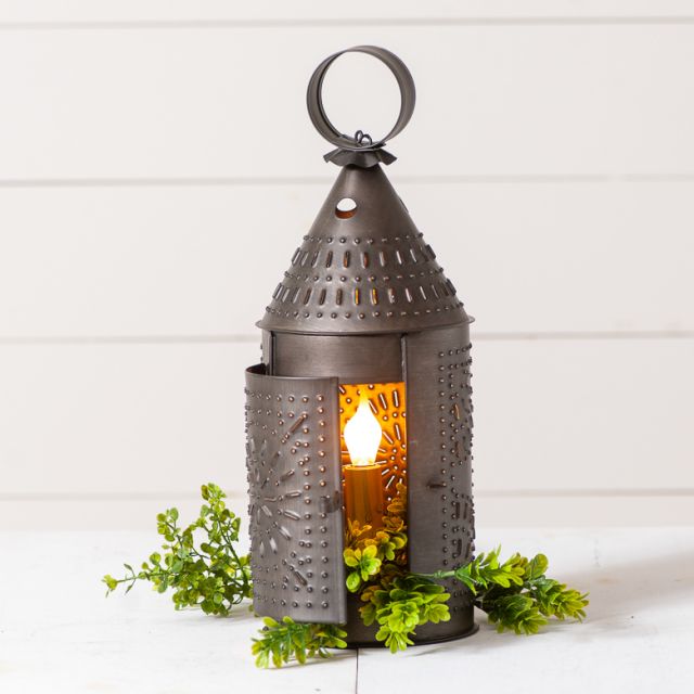 Punched tin lantern with candle ring in front of a white wall.