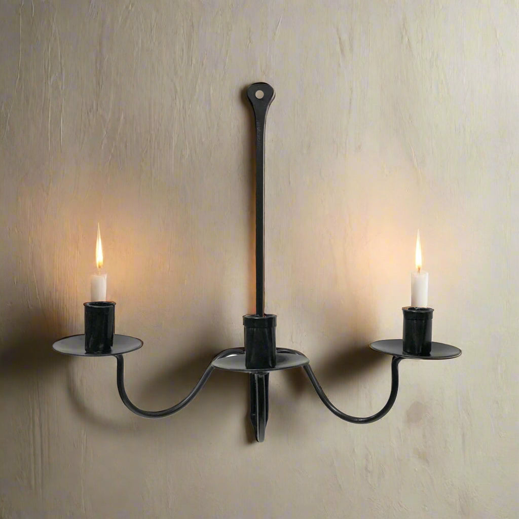 A black wrought iron hanging candle holder with three candle holders and a single central candle holder, all mounted to the wall.