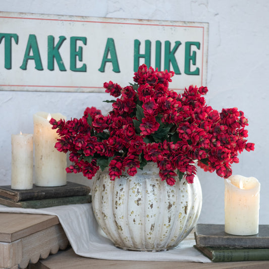 Red flowers in round vase with pillar candles and old books with tin sign in background.