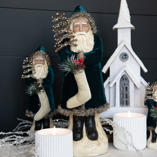 A set of three velvet Belsnickel figurines in a church setting, each with a unique facial expression, dressed in green and white holiday attire, with a decorative backdrop featuring a white church, greenery, and candles.