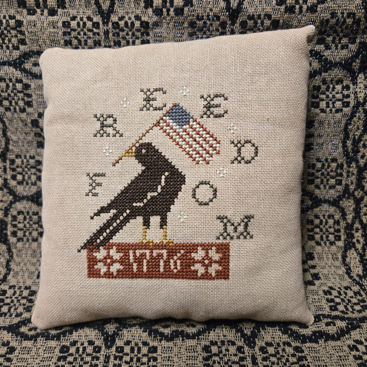 Cross-stitched pillow with a horse and flag design on a textured fabric background