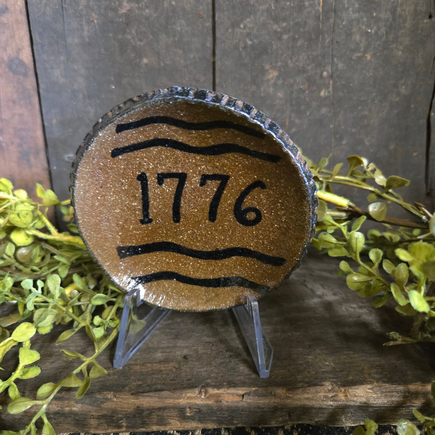 Decorative plate with '1776' on a wooden surface with greenery