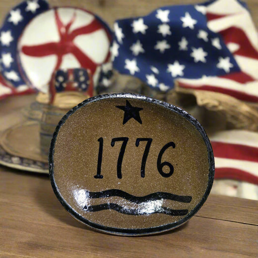 Decorative stone with '1776' on a wooden surface with American flags in the background