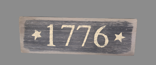 A rectangular wooden sign with the inscription '1776' in a heraldic font, surrounded by stars and asterisks on a dark background.
