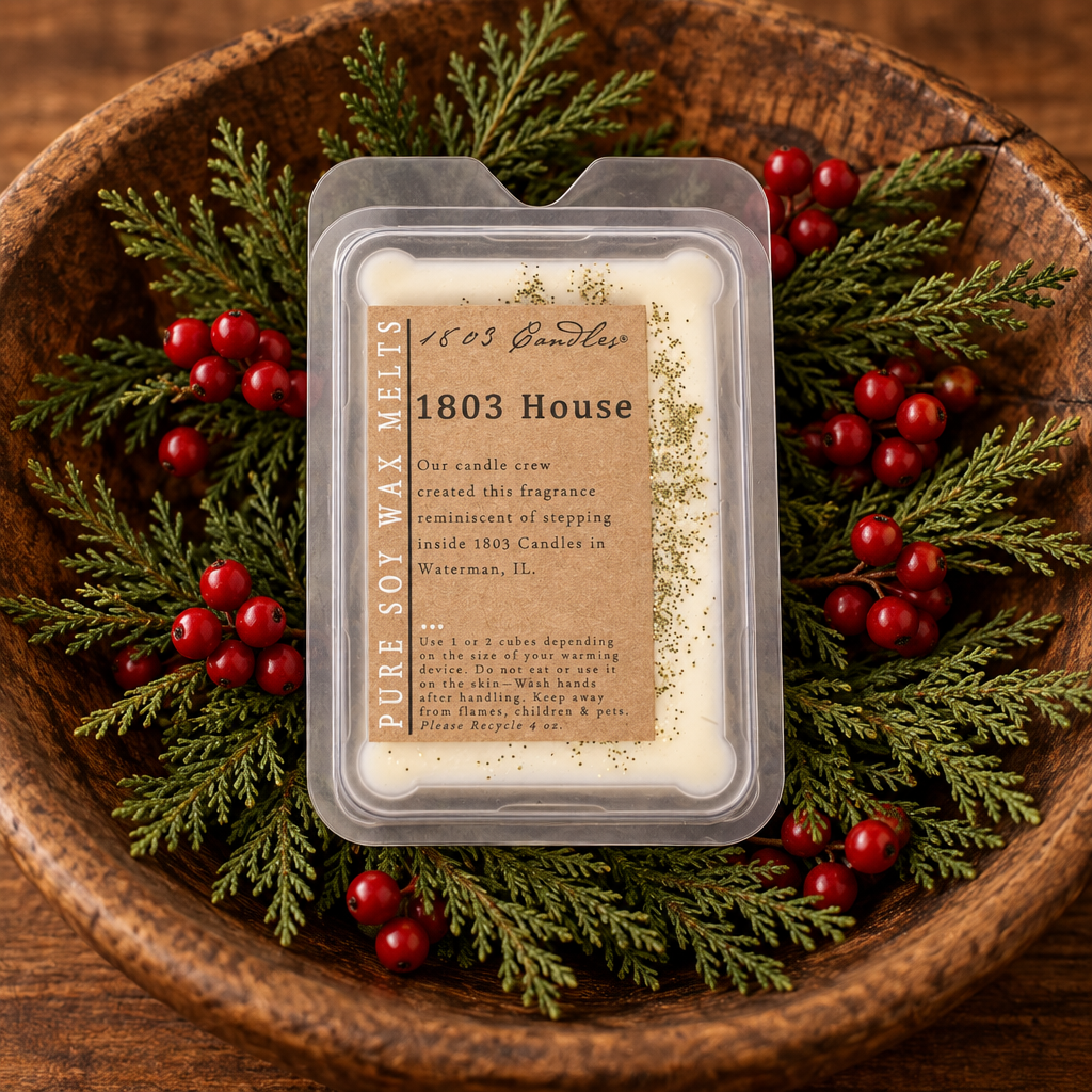 A packaged soy wax melt labeled '1803 House' by 1803 Candle Co., placed in a wooden bowl with evergreen branches and red berries.