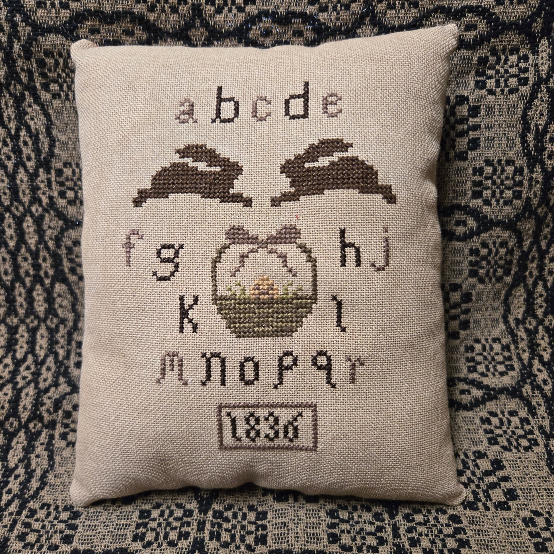 Decorative pillow with cross-stitched design on a textured fabric background