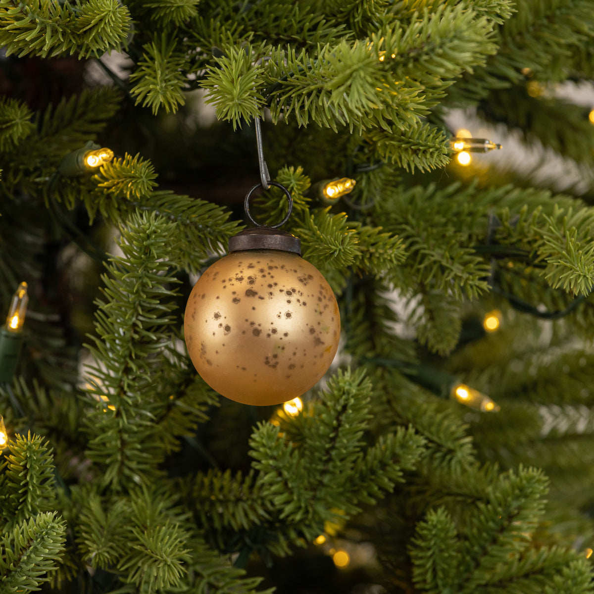 Gold ornament on a Christmas tree with lights