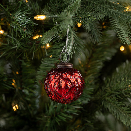 Red textured Christmas ornament on a tree with green leaves and blurred lights in the background