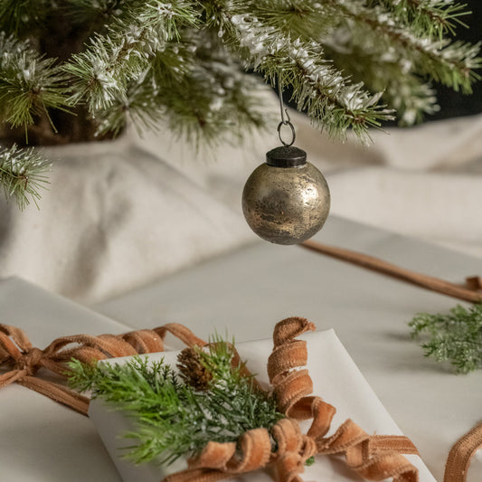 Decorative ornament hanging from a Christmas tree with a wrapped gift and ribbon in the foreground.