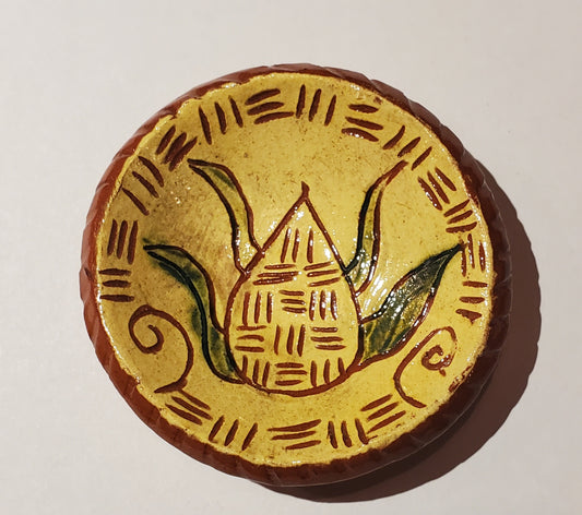 Round ceramic tile with a yellow center featuring a plant design, on a beige background