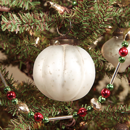 A white ridged glass ornament with a glossy finish, resembling a mercury-like effect, hanging from a Christmas tree with green and red ornaments.