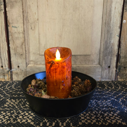 A burnt orange LED candle with a moving flame effect, placed in a black holder on a table with a lace tablecloth.