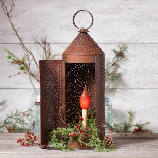 Decorative lantern with a red candle inside, surrounded by greenery on a wooden surface.