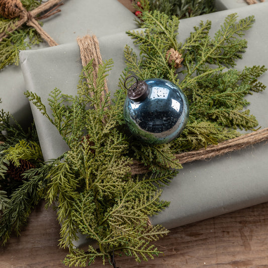 Gift wrapped in gray paper with greenery and a blue ornament on a wooden surface