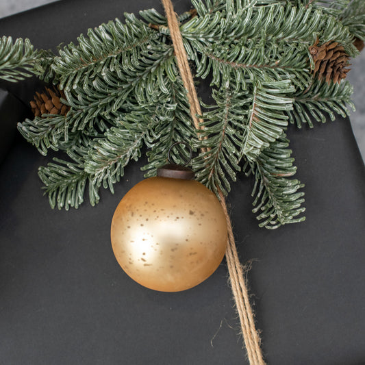 Gold Christmas ball ornament on a branch with pine cones against a dark background