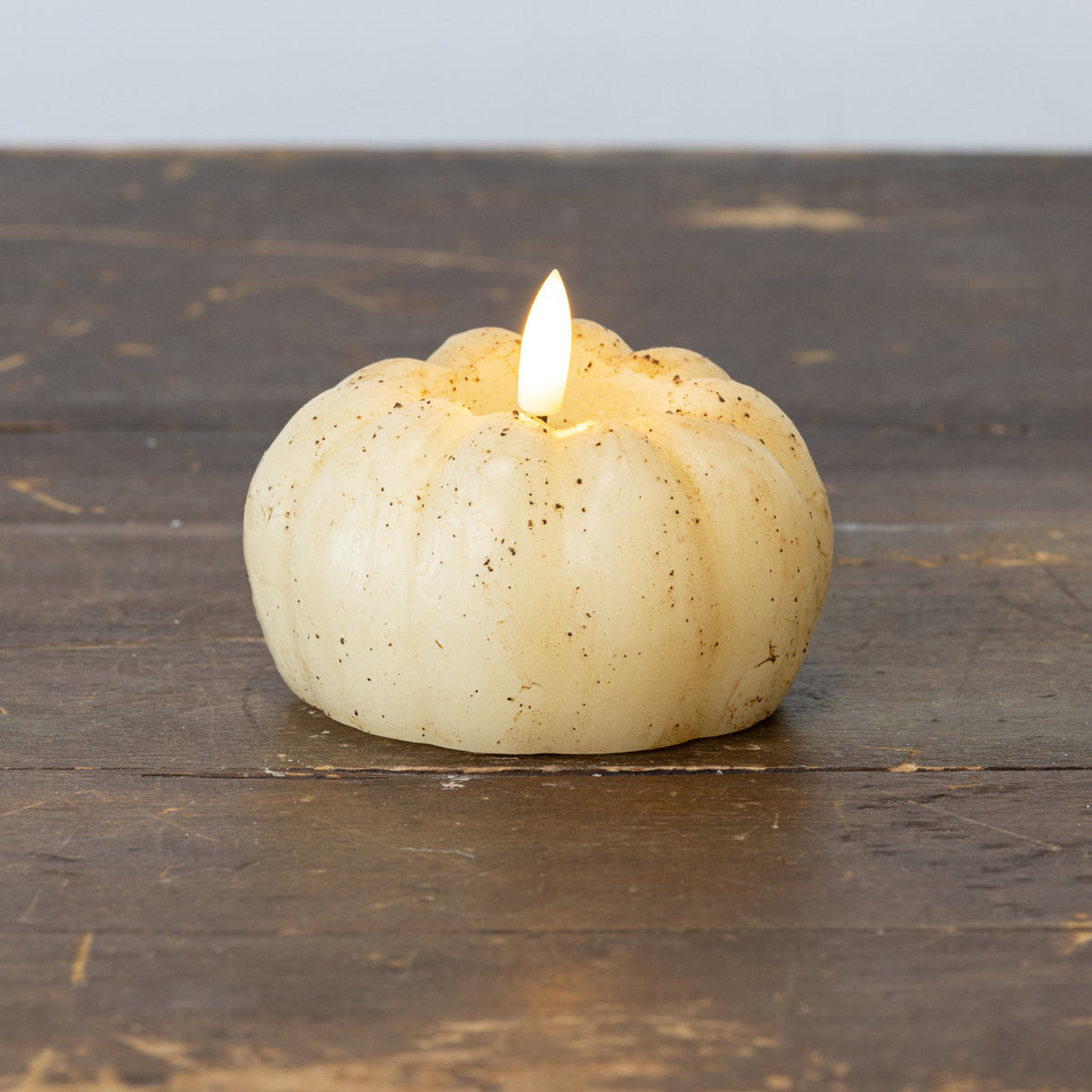 White pumpkin-shaped candle with a lit flame on a wooden surface