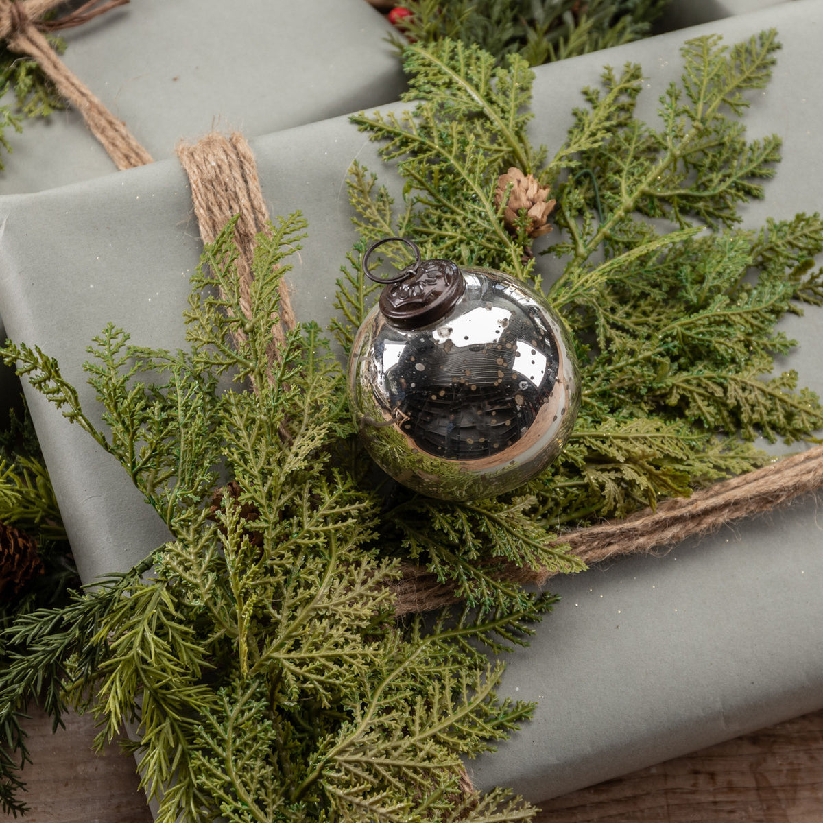 Silver ornament on a wrapped gift with greenery