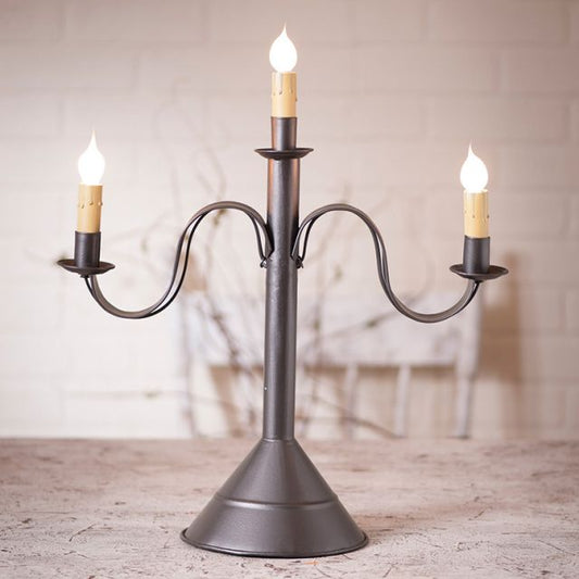Decorative black metal candelabra with three lit candles on a wooden surface.