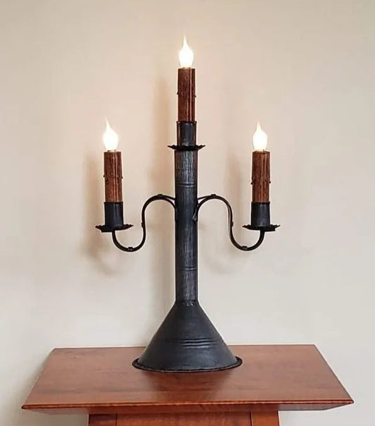 Black metal candelabra with three lit candles on a wooden surface against a plain background