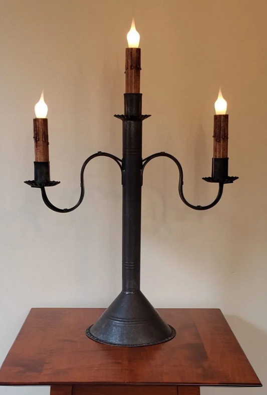 Black metal candelabra with three lit candles on a wooden surface against a plain background