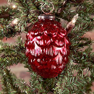 A red pine cone-shaped Christmas ornament hanging on a tree with green needles.