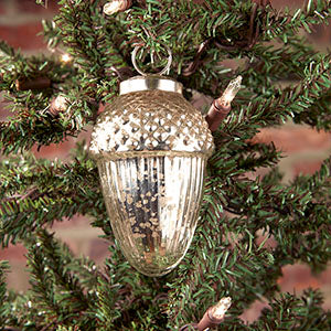 A silver acorn-shaped ornament with a geometric pattern hanging from a tree.