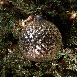 A 3-inch silver diamond-shaped mercury ornament with a glossy finish set against a backdrop of greenery.