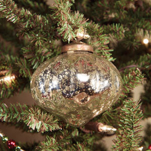 Small onion shaded ornament hanging from a lighted Christmas tree branch