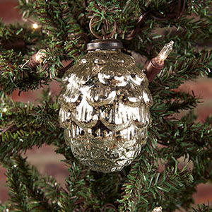 A silver pine cone-shaped ornament with intricate details and a reflective finish, hanging on a Christmas tree.