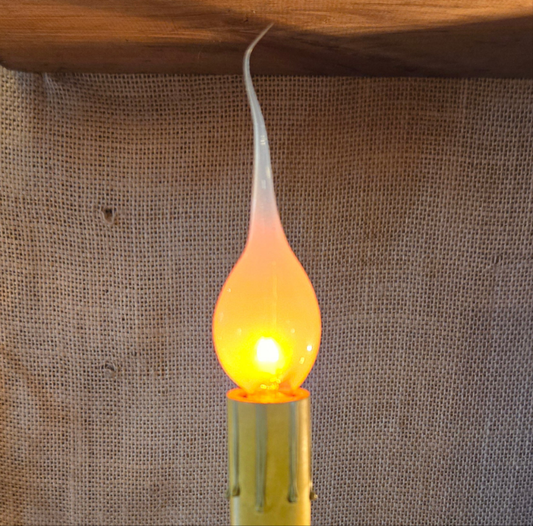 A 3 watt flicker-flame candle-light bulb glowing with a soft yellow light, inserted into a gold-colored candelabra base.