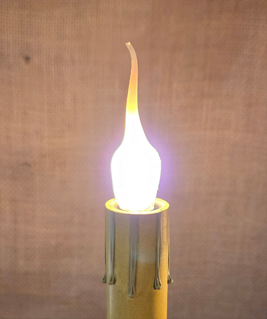 A small silicone bulb with a candelabra base, glowing with a warm white light, designed to mimic a candle flame.