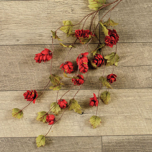 A bunch of vibrant red hops stems with green leaves, arranged on a wooden surface.
