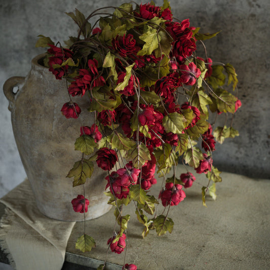 Artificial red flowers in a rustic vase against a textured wall.