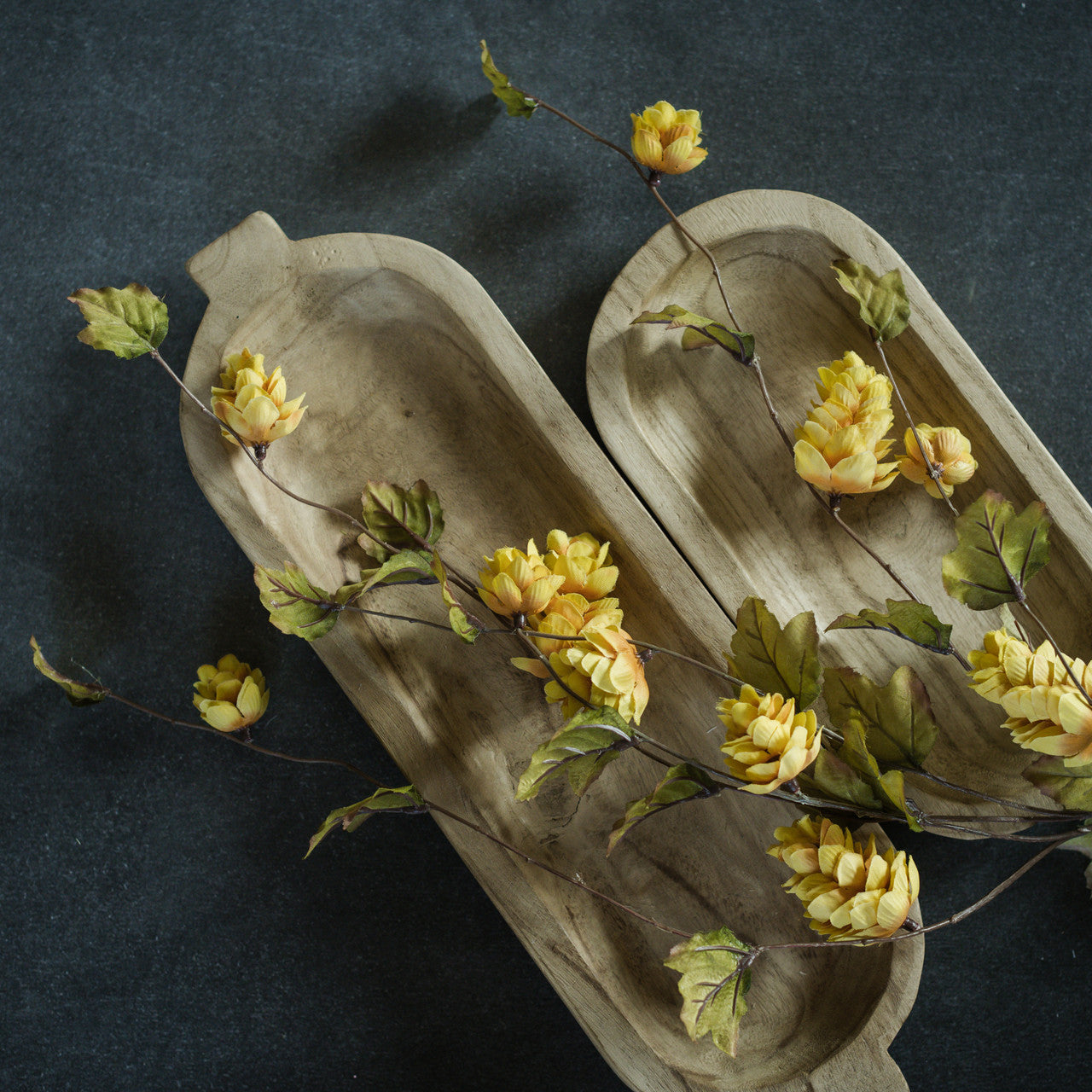 Artificial yellow hops stems arranged on a grey surface, with a wooden texture and lifelike appearance.