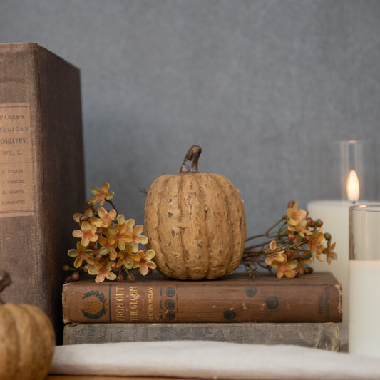 A beige tall pumpkin decoration placed on a surface with a book and a candle.