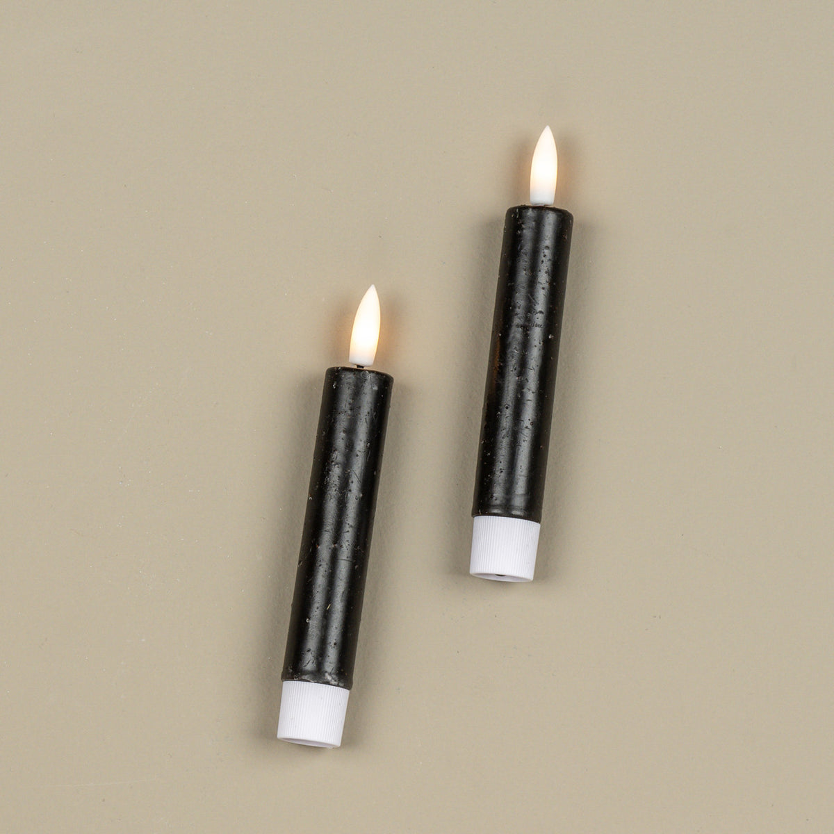 Two black candles with white bases and flames on a beige background