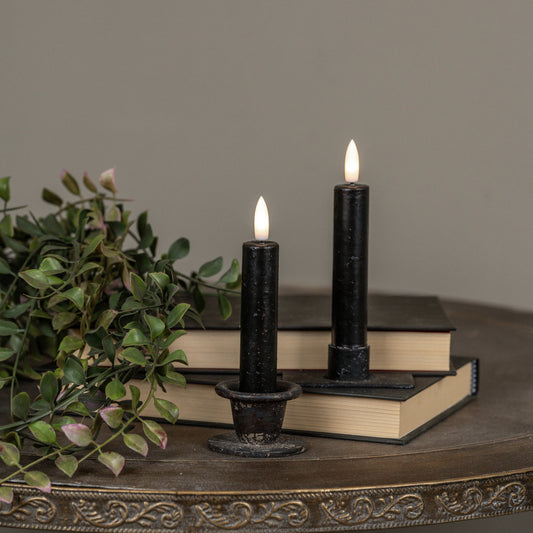 Two black candles with flame on a decorative surface with books and greenery.