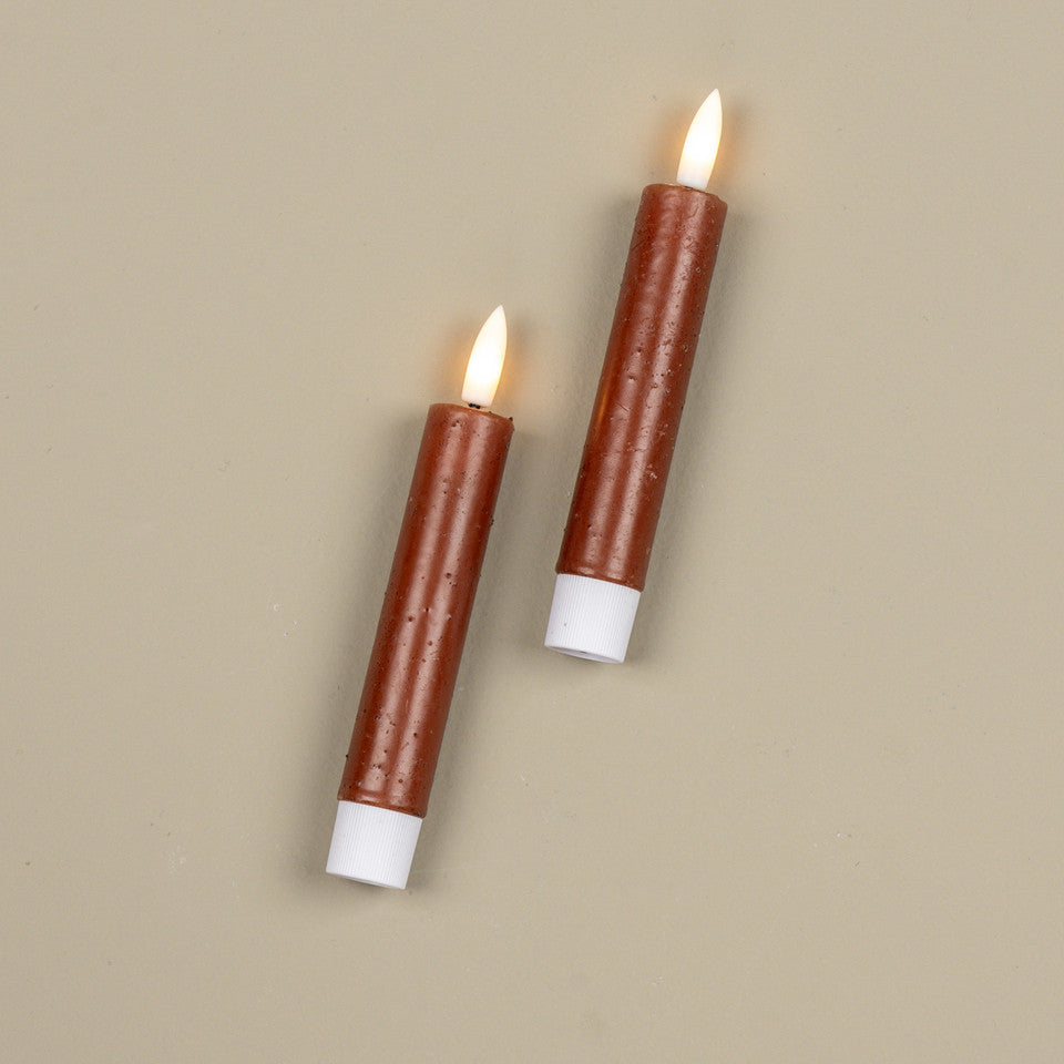Two brown candles with white bases on a beige background