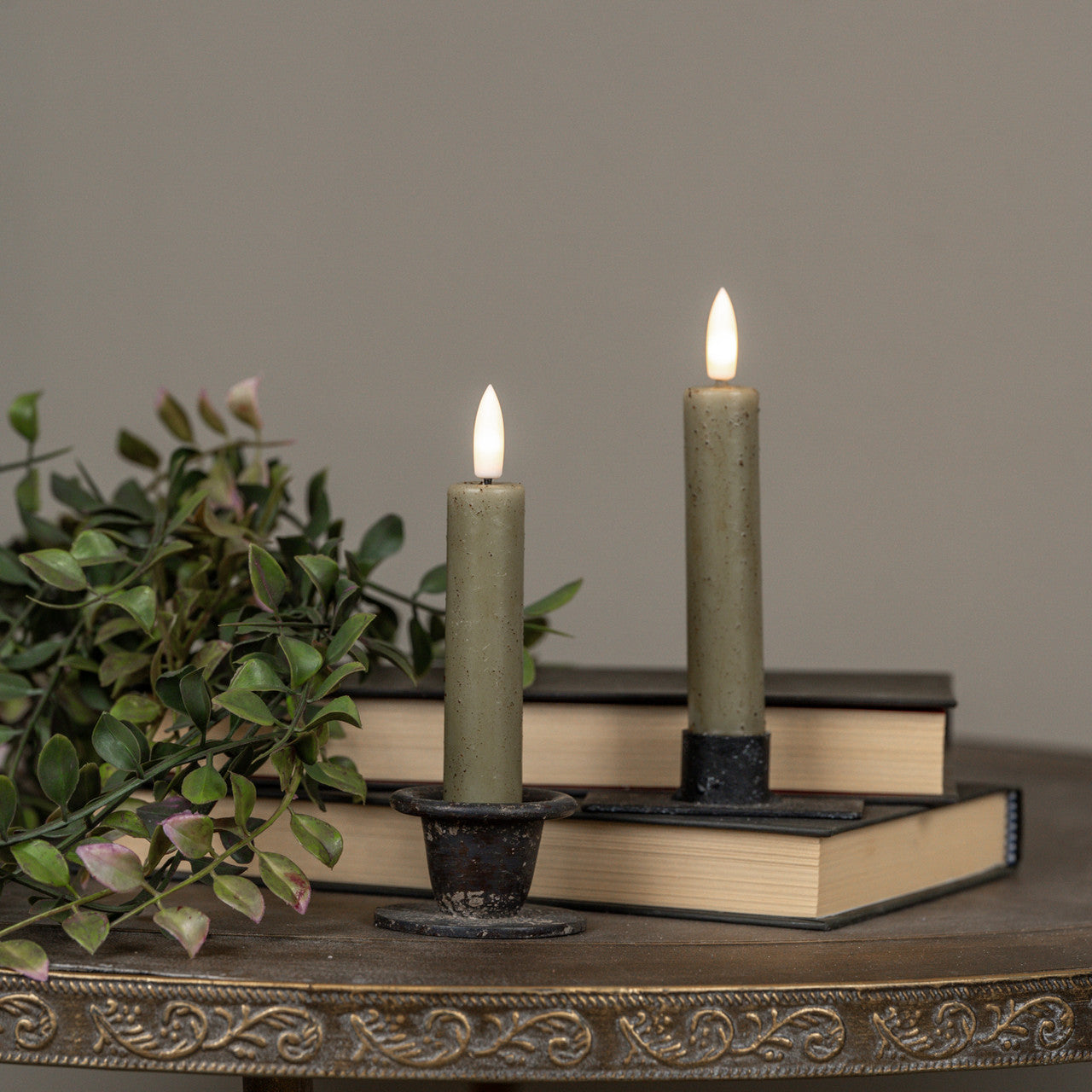 Two lit candles on books with a plant on a decorative surface.