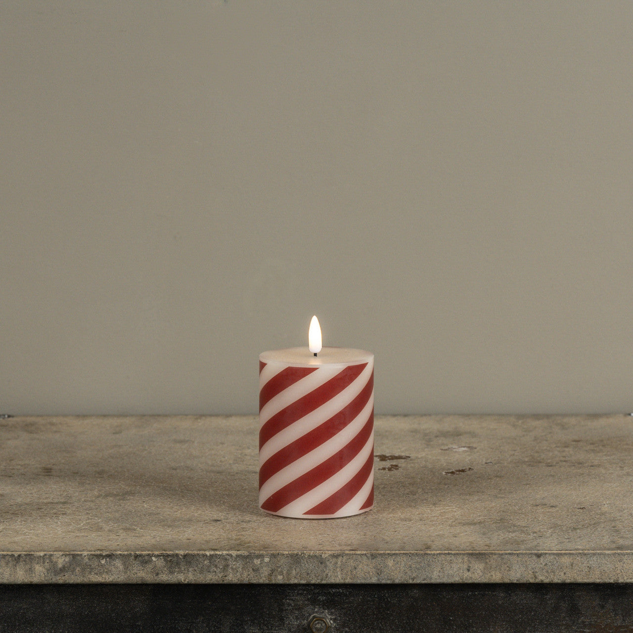 Red and white striped candle on a wooden surface with a gray background