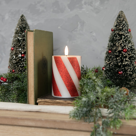 Candy cane pillar candle on mantle with bottlebrush trees, book and greenery.