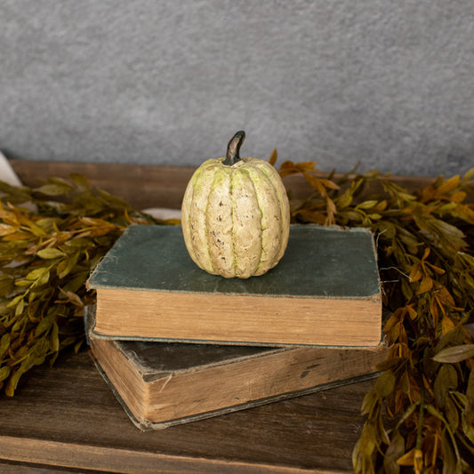A beige-colored pumpkin-shaped decoration placed on top of two books with a background of decorative leaves.